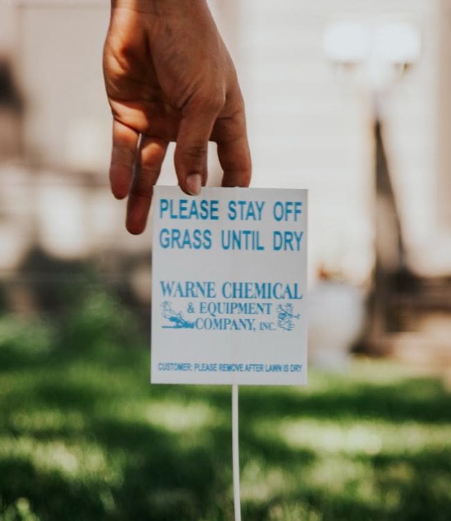 Warne worker placing a sign in lawn after spraying for weeds